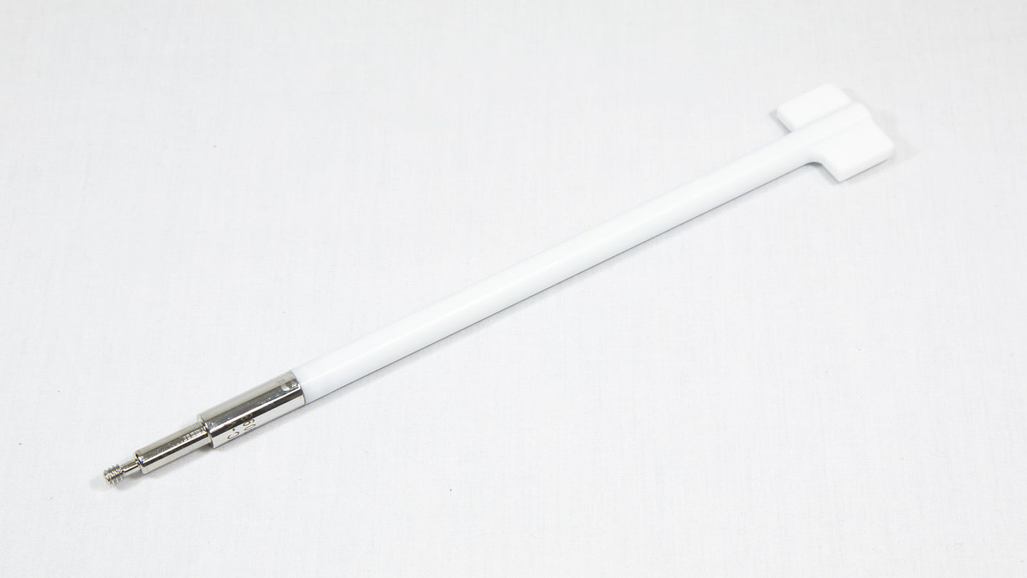 A white rod with a metal tip rests on a smooth white surface, highlighting its sleek design and minimalistic style.