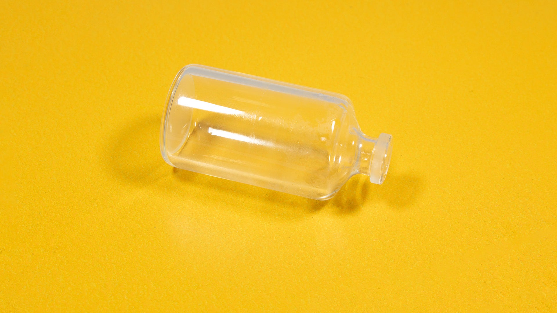 A clear glass bottle resting on a bright yellow surface, showcasing its transparency and shape.