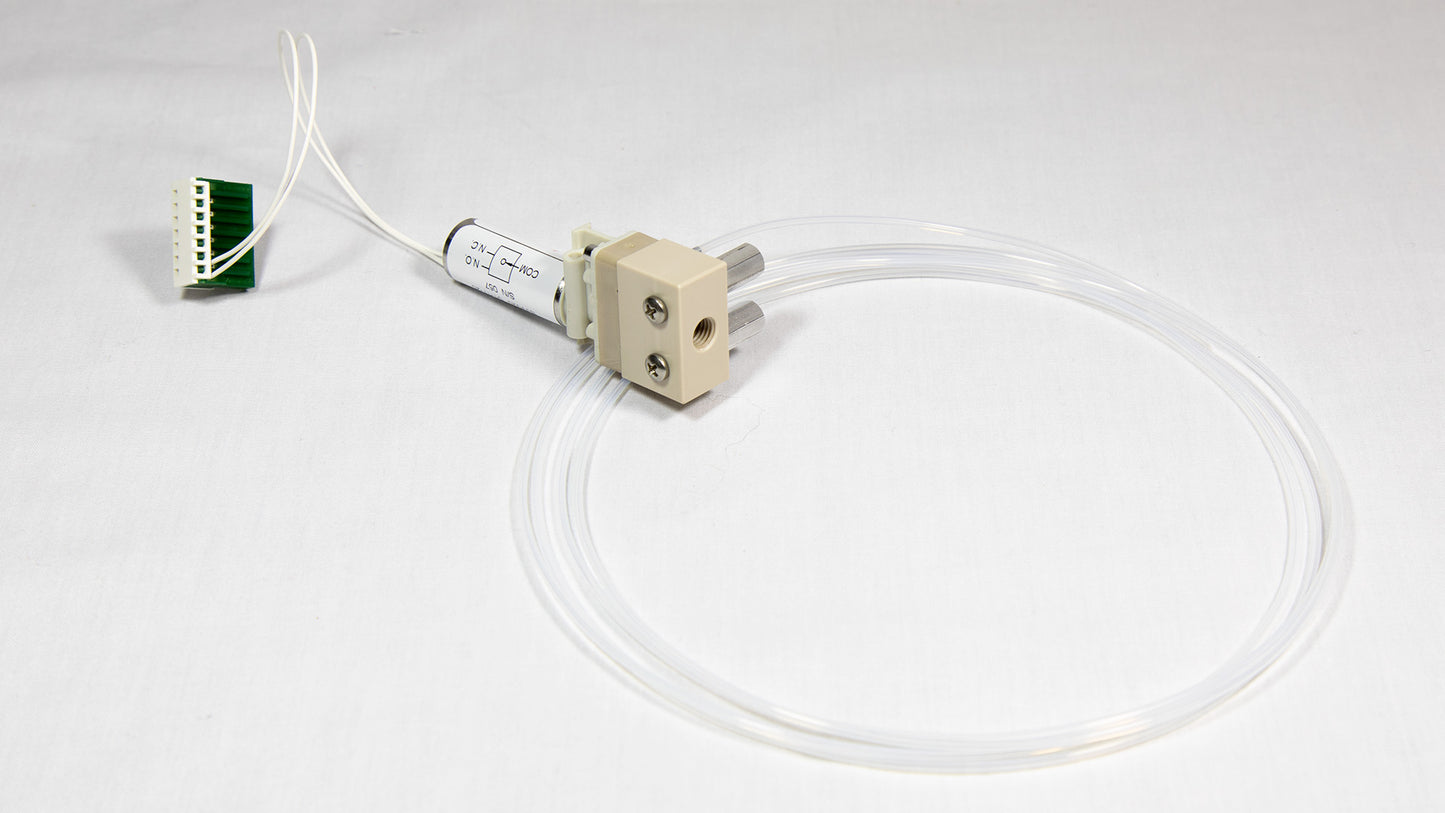 A small valve with clear tubing connected, along with an electronic wire, both resting on a neutral background.
