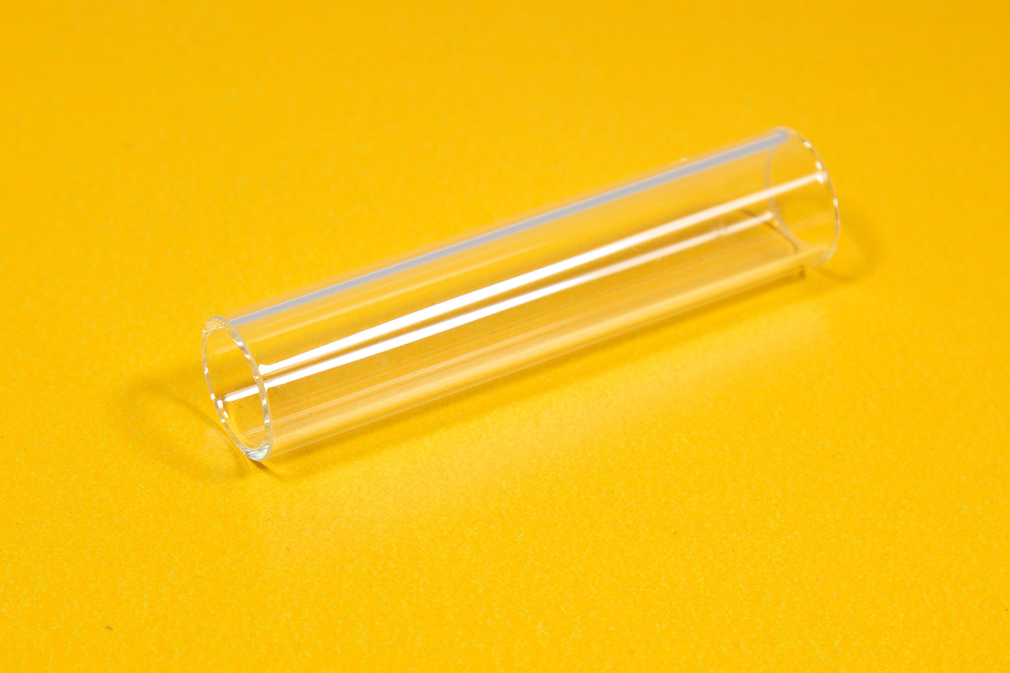 A clear tube resting on a bright yellow surface, showcasing its transparency and smooth texture.