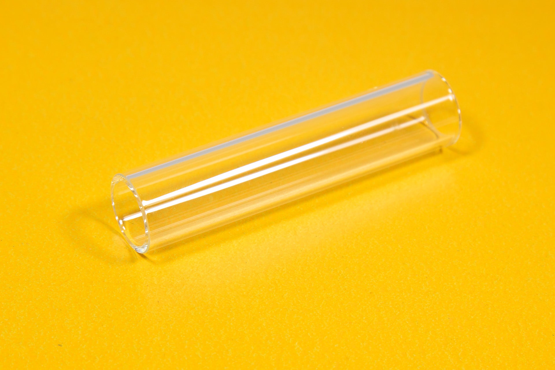 A clear tube resting on a bright yellow surface, showcasing its transparency and smooth texture.