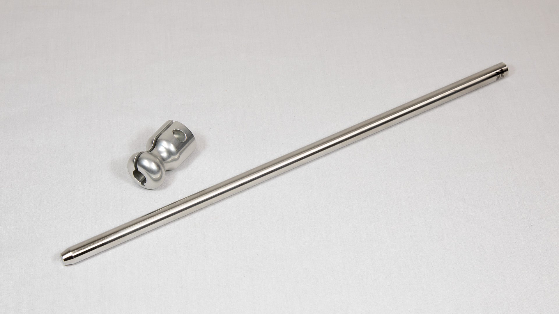 A stainless steel rod placed next to a clamp on a neutral background.