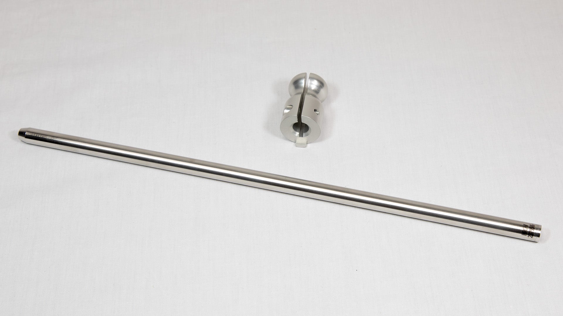 A stainless steel rod placed next to a clamp on a neutral background.