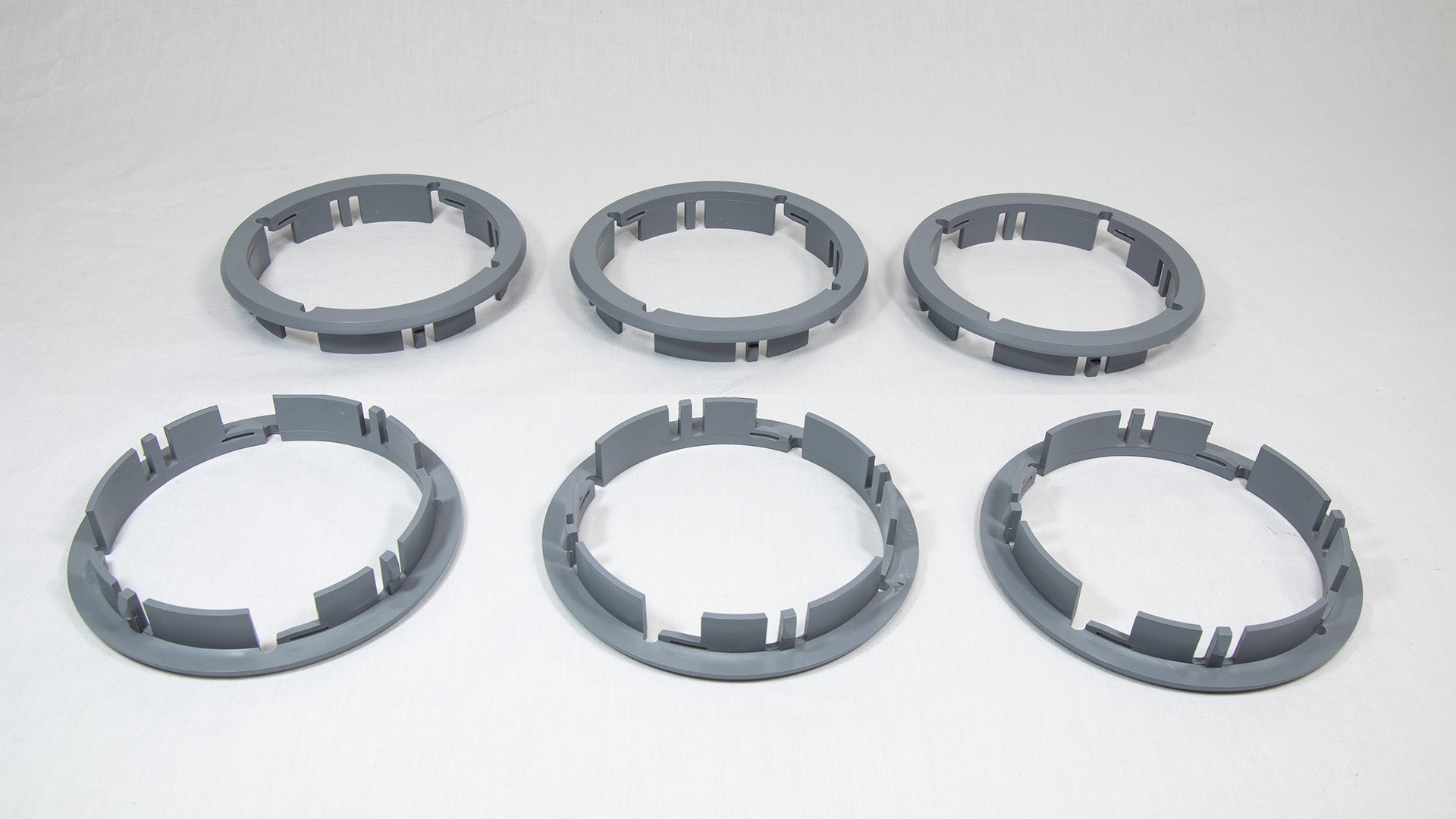 Six gray plastic rings arranged on a white surface, showcasing their circular shape and smooth texture.