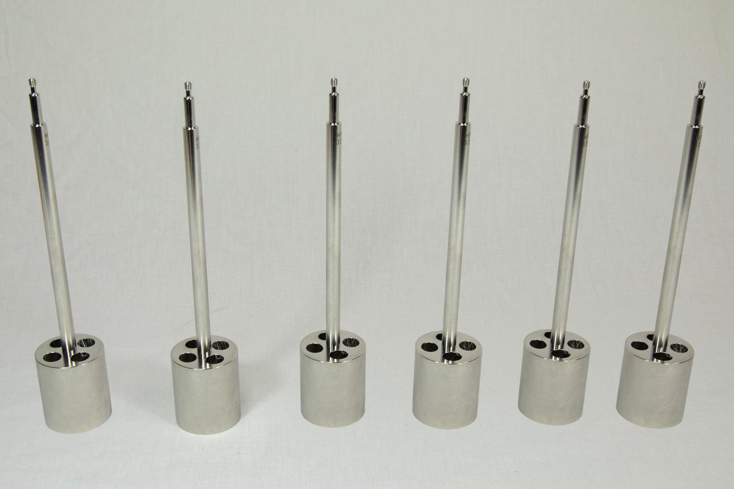 Set of six metallic cylindrical objects with threaded ends on a white background