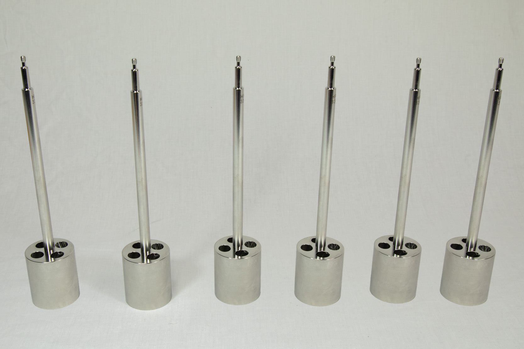 Set of six metallic cylindrical objects with threaded ends on a white background