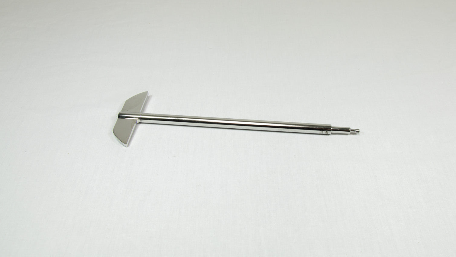 A stainless steel rod with a metal tip rests on a smooth white surface, highlighting its sleek design and minimalistic style.