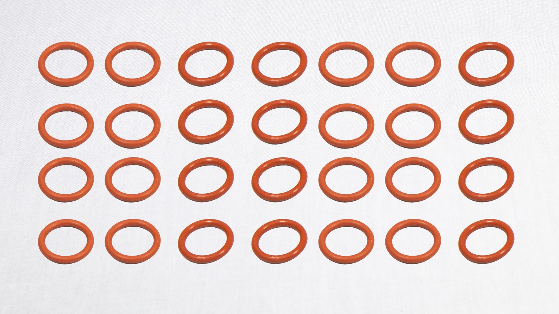 A group of orange rubber O-rings displayed on a plain white surface.